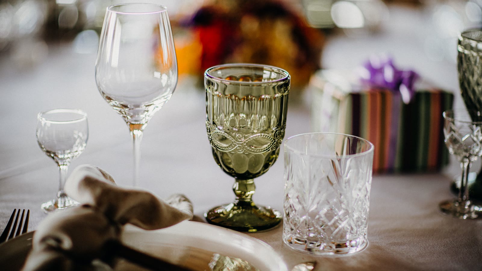 Flere forskellige glas opstillet ved samme kuvert på et dækket bord