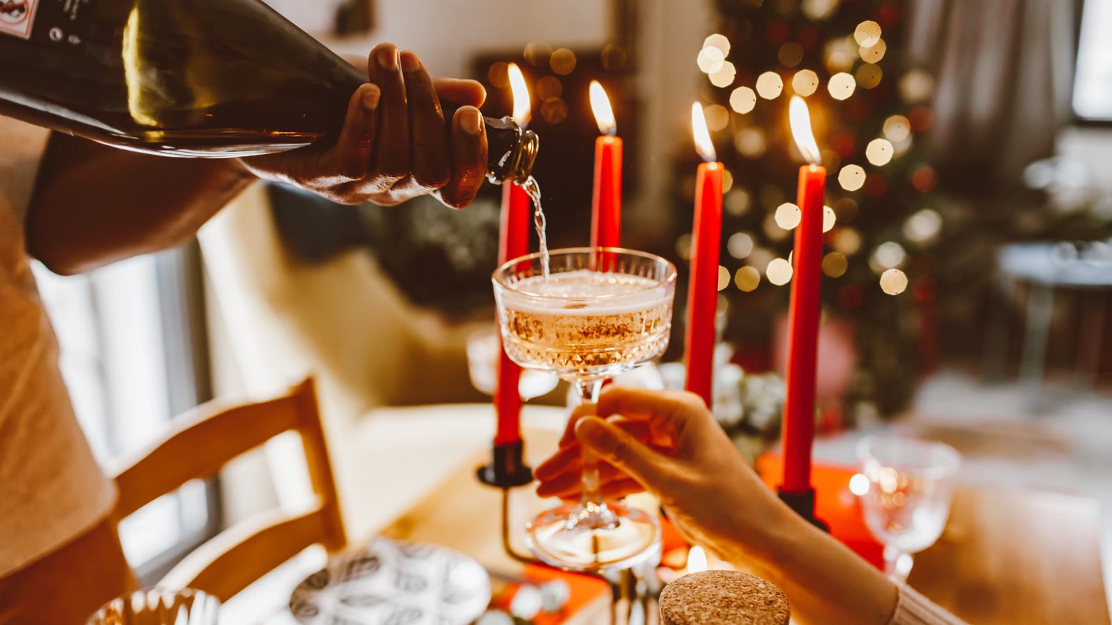 Julebord med røde stearinlys og glas, juletræ i baggrunden