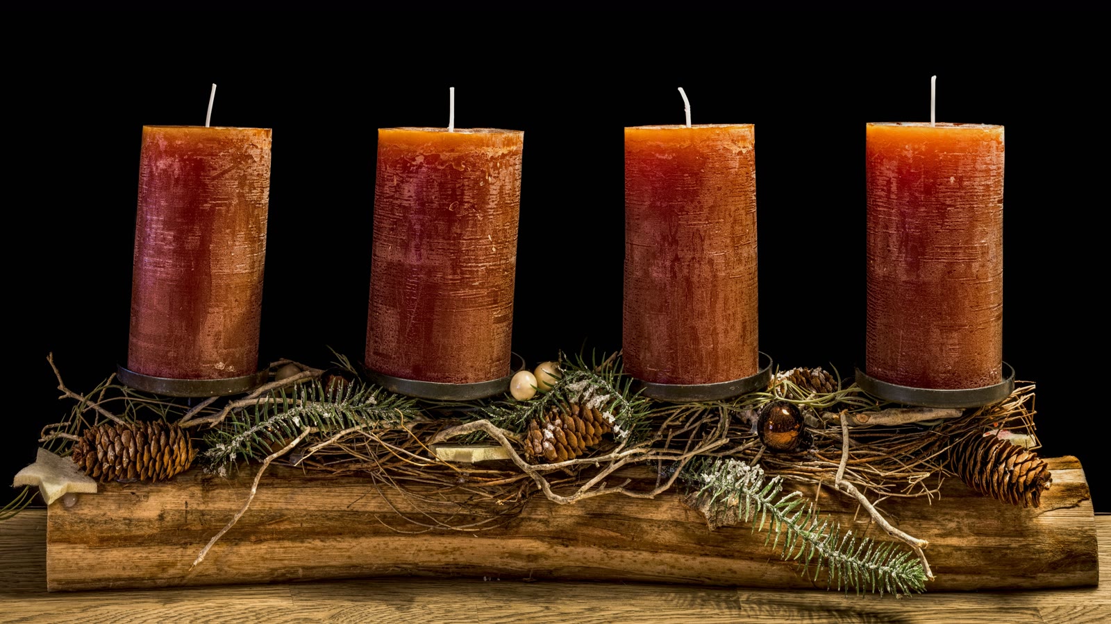 Juledekoration med fire rustikke bloklys på en gren med gran og kogler